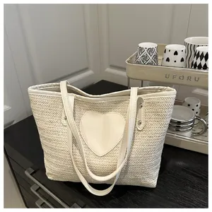 Gros plan du sac cabas tissé crème avec un patch cœur en cuir et rivets sur la lanière