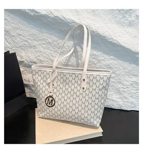 Detail view of M-pattern monogram tote bag featuring a gold logo pendant and leather handles