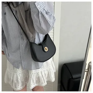 Détail du sac bandoulière demi-lune noir avec fermoir doré porté par un mannequin