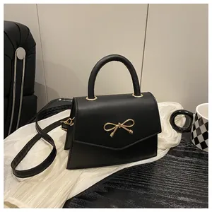 Close-up of the elegant golden bow clasp and matte leather texture on a black handbag