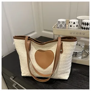 Détail du sac fourre-tout en paille tissée avec patch cœur marron et bandoulières en cuir PU