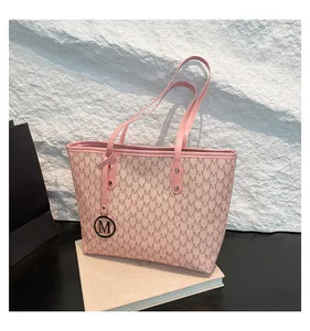 Close-up of pink monogram tote bag with gold metal M pendant and textured leather trim