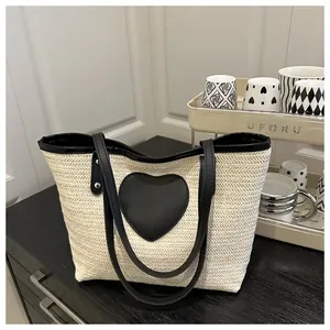 Détail du sac cabas en paille tressée avec un grand patch cœur noir et des anses doubles