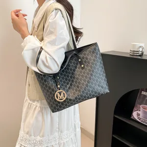 Black tote bag with M-letter pattern and gold metal pendant shown on shoulder