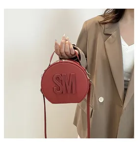 Close-up of circular red leather bag with embossed letters and double zipper details