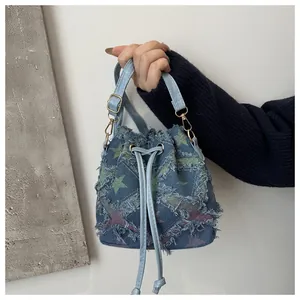 Détail du sac seau en denim bleu avec motif étoiles, bords effilochés et cordon de serrage