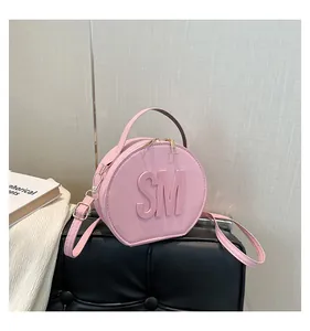 Close-up of pink round crossbody bag with SM embossed logo and golden hardware details