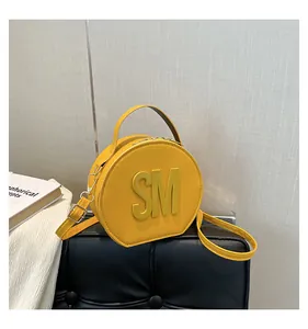 Detail view of yellow circular leather bag with bold 3D SM letter and silver hardware