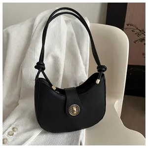 Détail du sac demi-lune noir avec fermoir doré circulaire et bandoulière à nœuds