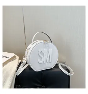 Detail of white round leather handbag with embossed SM letters and gold metal zippers