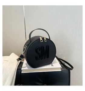 Macro view of black round crossbody bag showing textured PU leather and SM metal logo