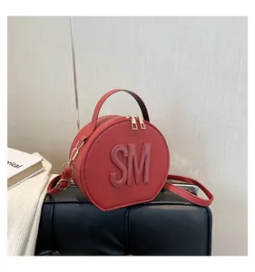 Detailed close-up of a red circular crossbody bag with embossed SM letters and gold zippers