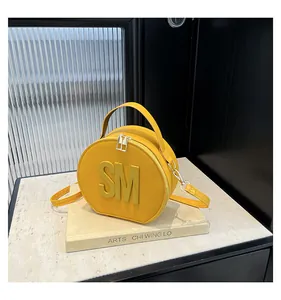 Macro shot of circular yellow leather bag detailing metal zippers and embossed letters