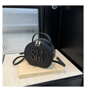 Macro detail of black circular bag with 3D SM logo and gold dual zipper closures