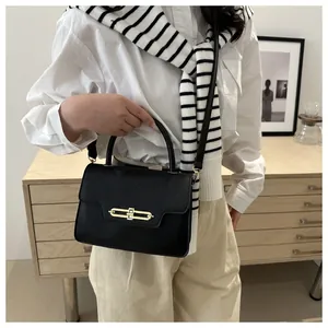 Detail view of black leather handbag with a textured flap and long golden metal clasp