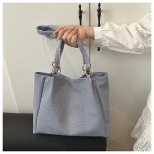 Detail of light blue denim tote bag showing golden ring hardware and detachable shoulder strap