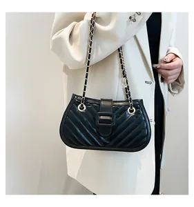 Détail d'un sac noir matelassé à chaîne avec boucle métallique sur un blazer blanc chic