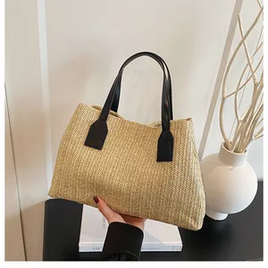 Close-up of woven straw tote bag featuring contrast black faux leather handles and V-shape knit