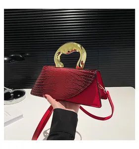 Detalle del bolso rojo con grabado de cocodrilo y asa artística de metal dorado