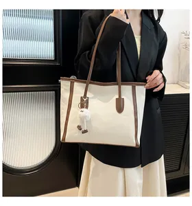 Detail of cream tote bag with brown straps and white plush monster charm on black blazer