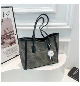Detail of dark grey tote bag featuring contrast black trim and white plush pendant