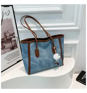 Detail of denim tote bag with brown trim and plush charm on a white display stand
