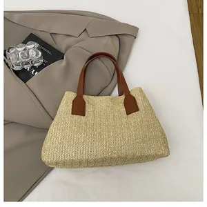 Close-up of a straw woven tote bag with premium brown leather handles on a styled background