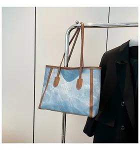 Detail of blue denim tote bag with brown leather trim hanging on a metal rack