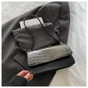 Détail du rabat en cuir croco noir avec liseré doré sur un sac à bandoulière chic