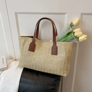 Handwoven straw tote bag with brown faux leather handles and a herringbone texture