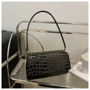 Détail d'un sac à bandoulière noir à motif crocodile et détails dorés sur étagère