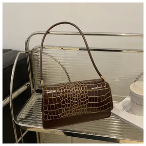 Gros plan sur la texture crocodile dorée et le rabat en cuir d'un sac à bandoulière brun