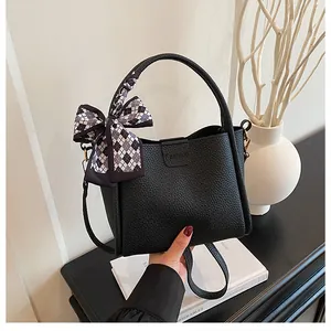 Detail of black pebbled leather bucket bag with a fashion logo and decorative plaid scarf