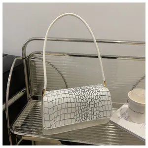 Détail d'un sac à bandoulière blanc avec motif crocodile noir sur un support en métal