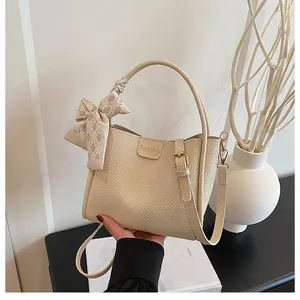 Detail view of cream bucket bag featuring lychee texture and silk scarf handle decoration
