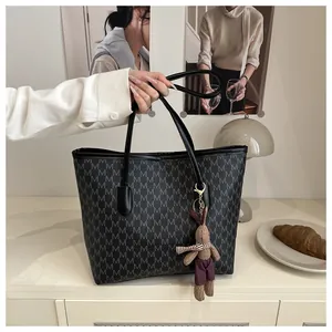 Detail of black tote bag with M letter prints and a brown bunny charm on beige surface
