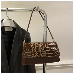 Détail du sac à bandoulière marron foncé à motif crocodile sur un cintre