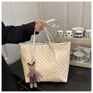 Detail of beige tote bag with M-letter monogram print and cute rabbit pendant