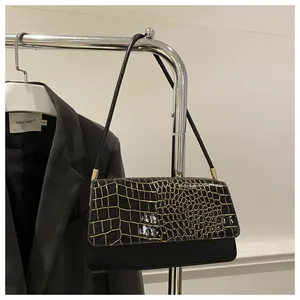 Détail du sac sous le bras noir avec rabat texture crocodile doré et fine bandoulière
