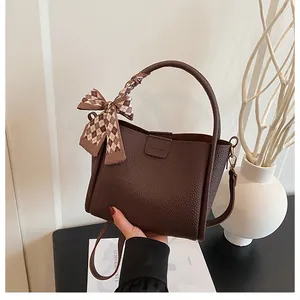 Close-up of dark brown bucket bag featuring lychee grain leather and a silk scarf bow