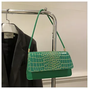 Détail du sac à rabat vert texture crocodile avec boucles dorées et bandoulière
