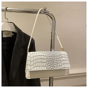 Détail d'un sac à bandoulière blanc à motif crocodile suspendu sur un cintre