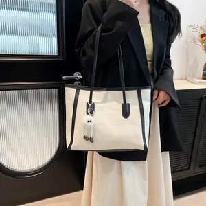 Minimalist beige tote bag with black trim and a cute plush monster charm accessory