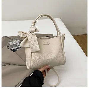 Detail of cream bucket bag featuring lychee texture and decorative checkered bow scarf