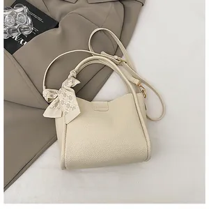 Detail of cream bucket bag with pebbled leather, metal snap, and plaid ribbon bow
