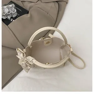 Close-up of beige bucket bag showing textured pebble leather and decorative plaid silk scarf