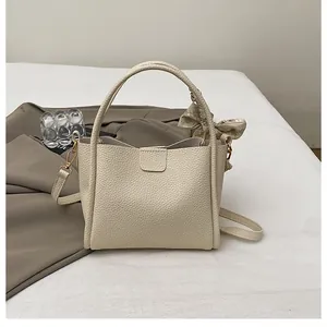 Close-up of litchi texture leather bucket bag with decorative silk scarf and golden hooks