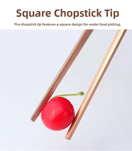 Close-up of rose gold stainless steel chopsticks with square tips holding a cherry