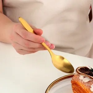 Elegant matte gold stainless steel dessert spoon held over a refined sweet treat