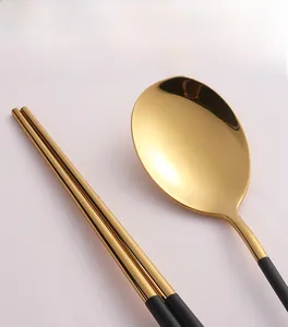 Détail macro d'un ensemble cuillère et baguettes en acier inox doré et noir poli